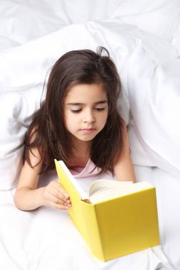 Güzel küçük bir kız okuma kitabı beyaz yatakta