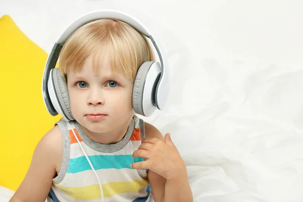 Lille dreng sidder med hovedtelefoner i hvid seng - Stock-foto