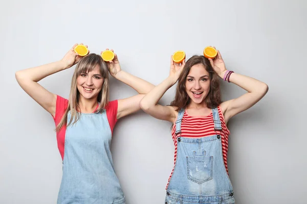 Dvě mladé ženy s oranž na šedém pozadí — Stock fotografie