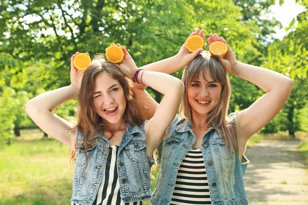 Duas jovens com frutas laranja no parque — Fotografia de Stock