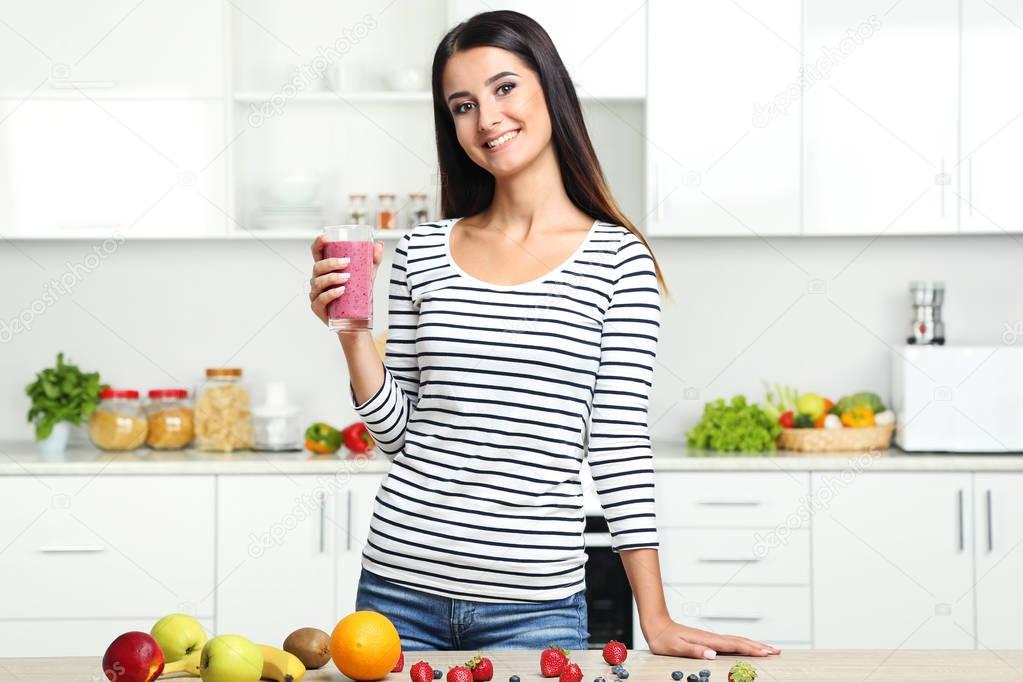 Beautiful young woman drinking smoothie in the kitchen