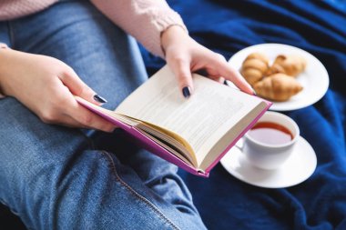 Fincan çay ve kitap üzerinde mavi kareli oturan kadınla