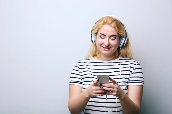 Mujer joven escuchando música con auriculares sobre fondo gris — Foto de Stock