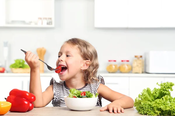 Menina comendo salada na cozinha — Fotografia de Stock