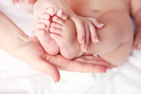 Pies de bebé recién nacidos en las manos de la madre en la cama blanca —  Fotos de Stock