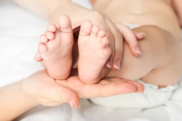 Bebé recién nacido pies en las manos de la madre en la cama blanca —  Fotos de Stock