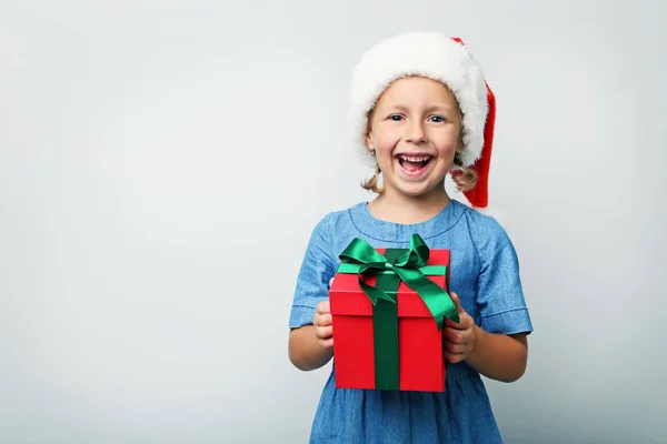 Retrato de menina no chapéu de santa e caixa de presente no backgr cinza — Fotografia de Stock