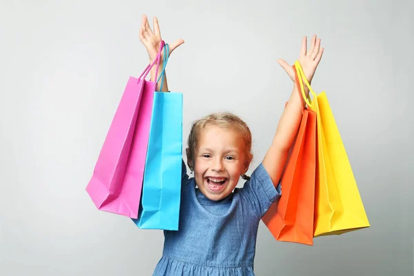 Little girl gazdaság bevásárló táskák, a szürke háttér portréja — Stock Fotó