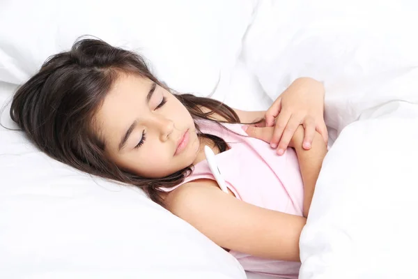 Petite fille malade avec thermomètre dans un lit blanc — Photo