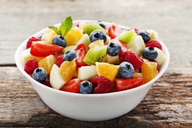 Gri ahşap masa üzerinde kase taze meyve salatası