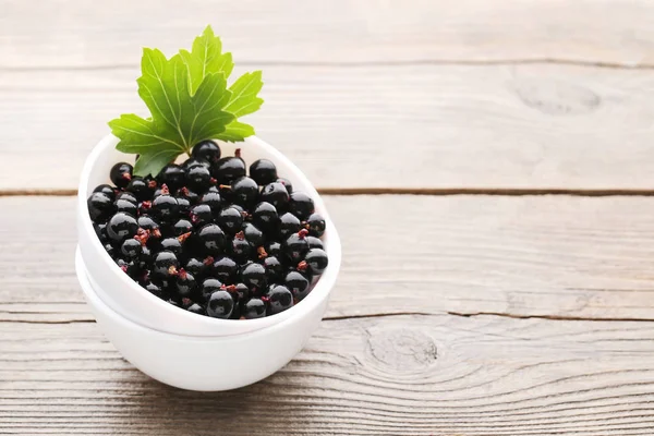 Black currants in bowl with leaves — Stock Photo, Image