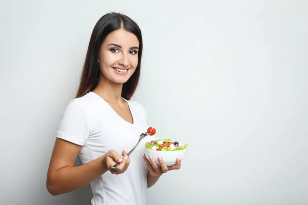 Jovem com salada de legumes em tigela no fundo cinza — Fotografia de Stock