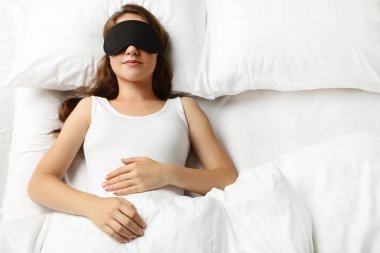 Genç kadın eyemask beyaz yatakta yatıyor