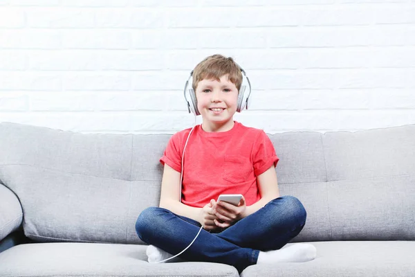 Портрет молодого хлопчика з навушниками та смартфоном на сірому софі — стокове фото