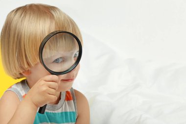 Beyaz yatakta oturmuş büyüteç ile küçük çocuk