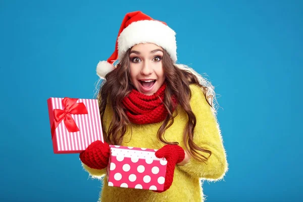 美丽的年轻女孩在圣诞老人帽子与礼物箱子在蓝色 backgrou — 图库照片