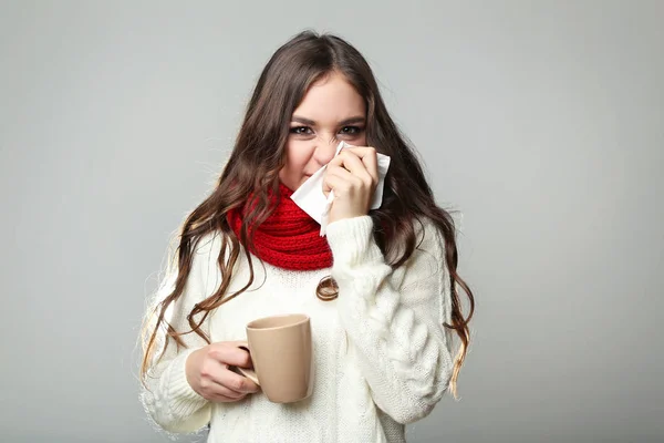 Krankes junges Mädchen mit Taschentuch und Tasse Tee auf grauem Rücken — Stockfoto