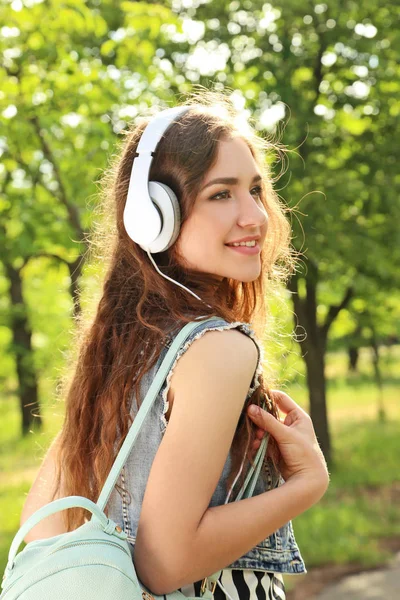 Πορτρέτο της νεαρής γυναίκας με τα ακουστικά και το σακίδιο στο πάρκο — Φωτογραφία Αρχείου