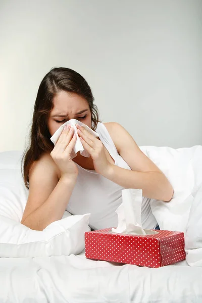 Sick young woman sneezing in tissue in white bed — Stock Photo, Image