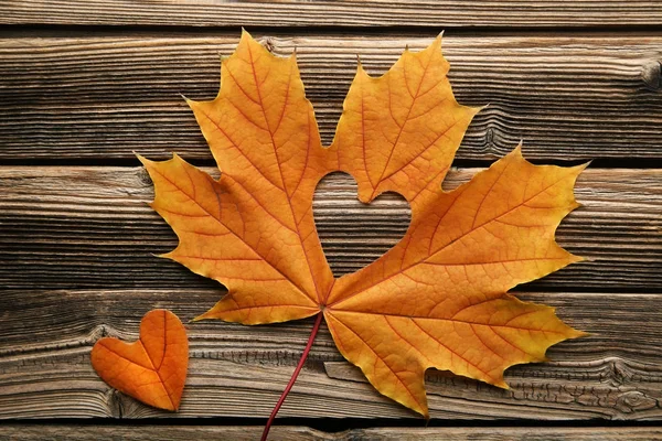 Dry maple leaf with heart on brown wooden table