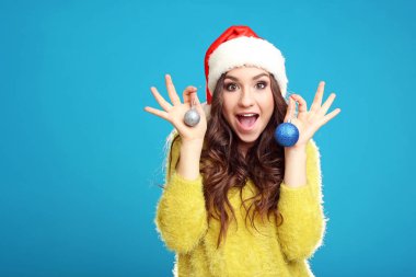 Noel Baba şapkası baubles mavi arka plan üzerinde tutan genç kız güzel