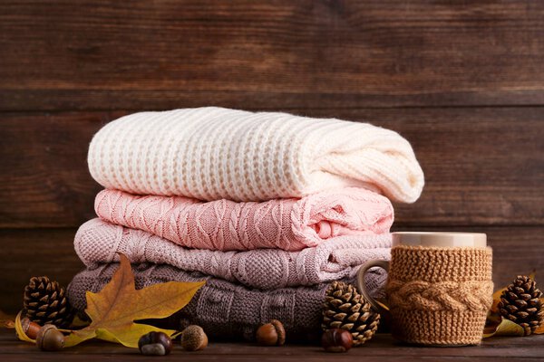 Stack of knitted sweaters with cup of tea and autumn leafs