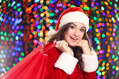 Noel Baba şapkası ışıklar arka plan üzerinde alışveriş torbaları ile genç kadın