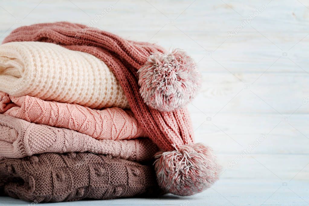 Stack of knitted sweaters and scarf on wooden table