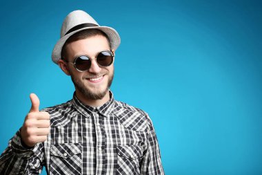 Güneş gözlüğü ve şapka mavi arka plan ile genç adam portresi