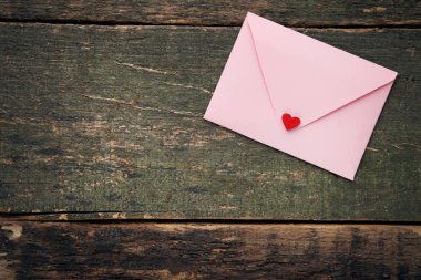 Gri ahşap masa üzerinde pembe zarf ile kırmızı kalp