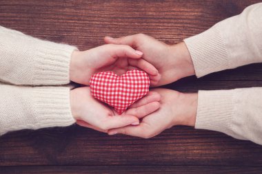 Kahverengi zemin üzerine kırmızı kumaş kalp tutan kadın ve erkek el