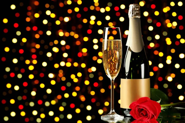 Champagne bottle with glass and red rose on lights background