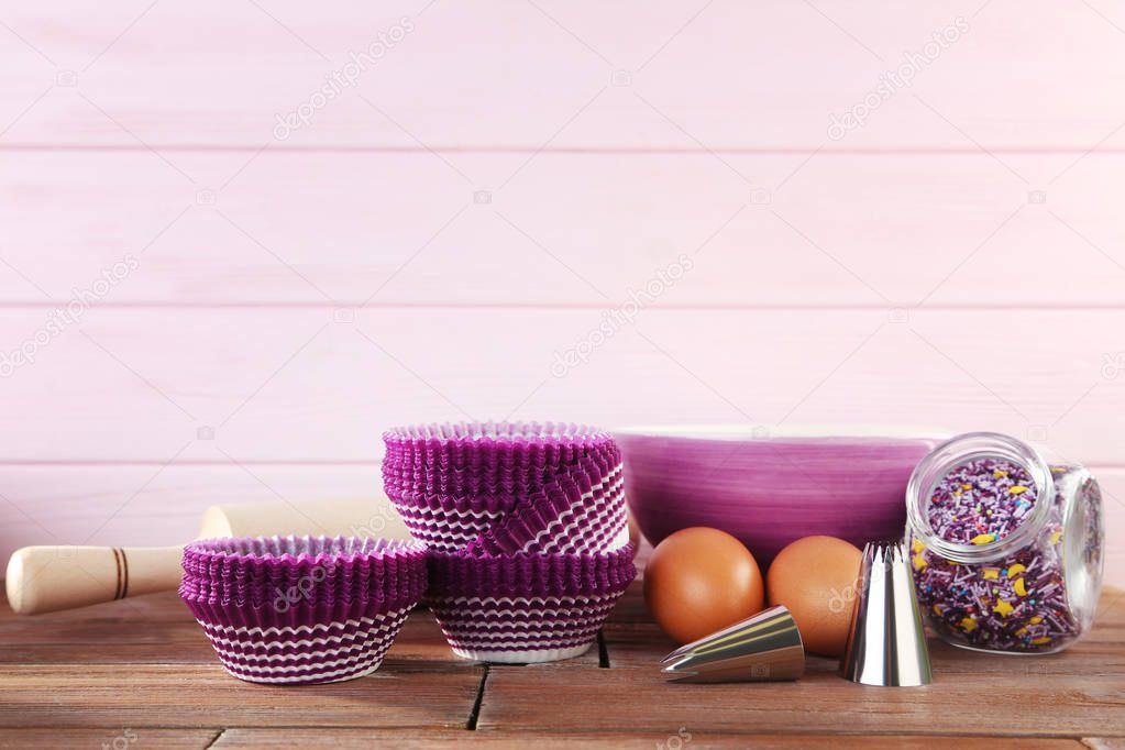 Empty cupcake cases with bowl of flour and eggs on wooden table