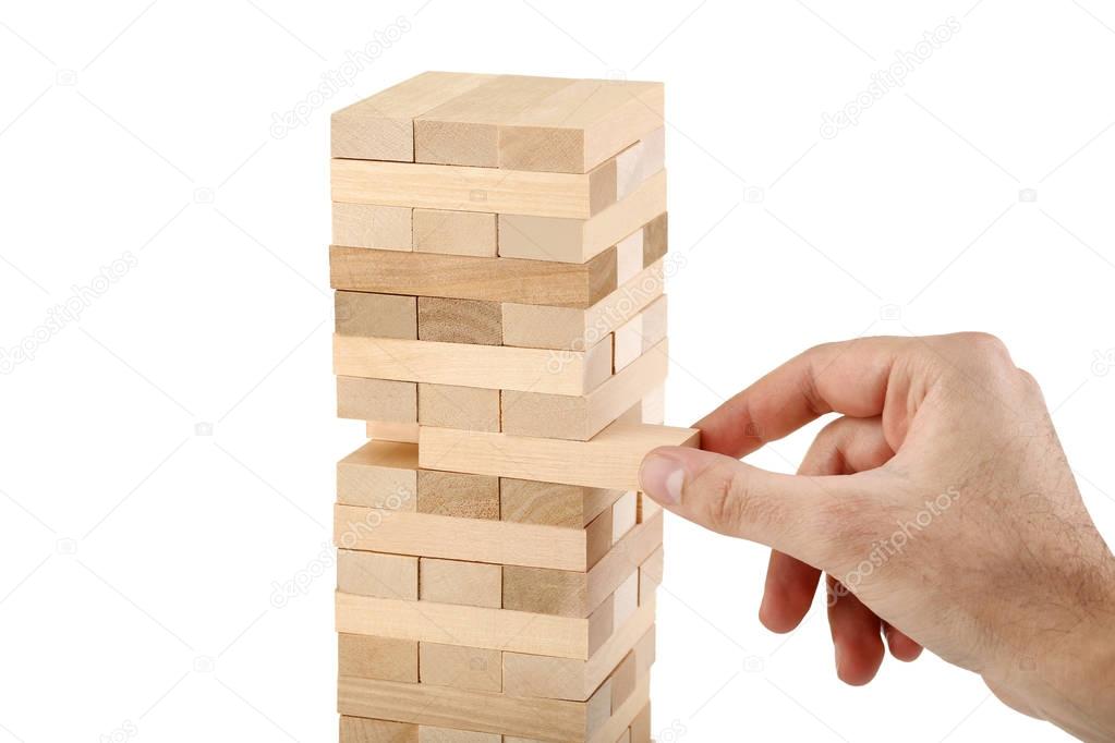 Male hand playing wooden blocks tower game Jenga on white background