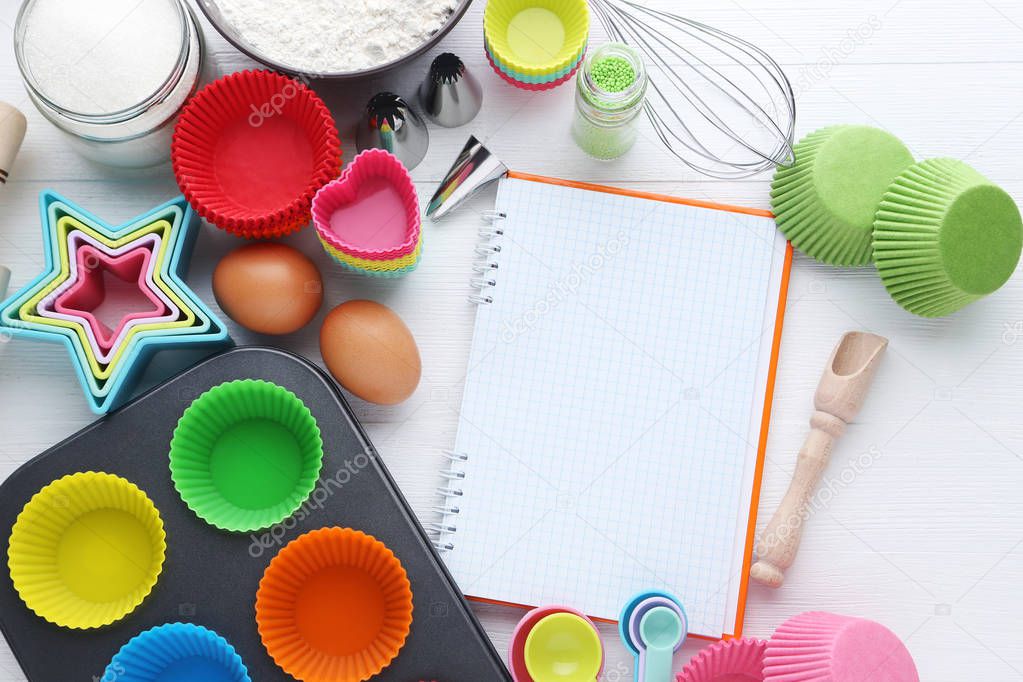 Top view of empty cupcake cases with different kitchen utensils on wooden table