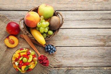 Kaşık ve sepet gri ahşap masa üzerinde kase meyve salatası