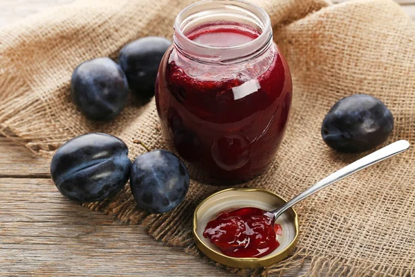 Plum jam in jar with spoon on grey wooden table