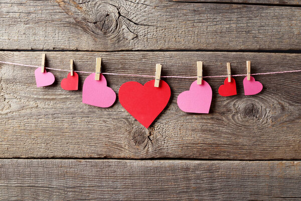 Red and pink paper hearts hanging on wooden background