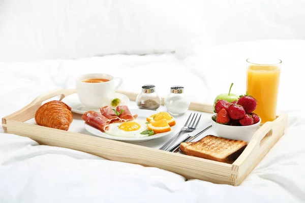 Tasty breakfast in bed on wooden tray