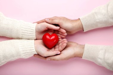 Pembe arka plan üzerinde kırmızı kalp tutan kadın ve erkek el