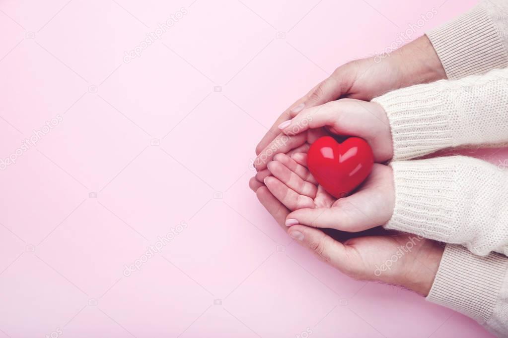 Female and male hand holding red heart on pink background