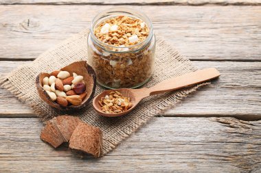 Gri ahşap masa üzerinde kaşık ve cam kavanoza lezzetli granola