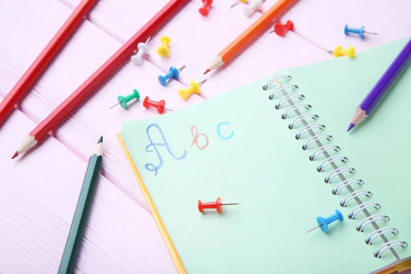 Handwritten letters ABC in notebook with stationery on pink wooden table