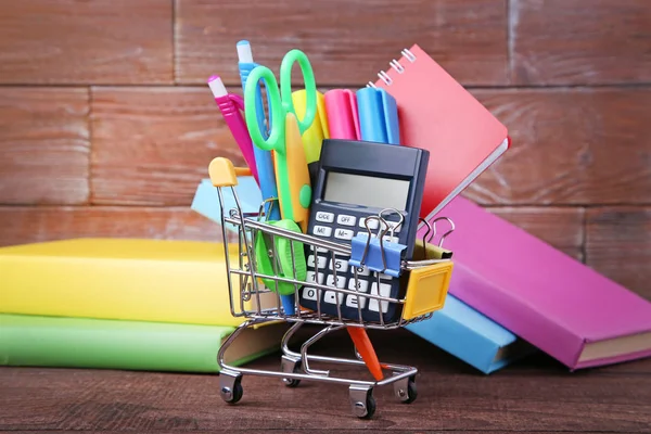 Shopping cart with school supplies with books on wooden table