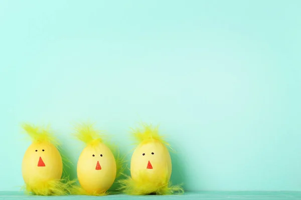 Yellow eggs with funny chicken faces on mint background