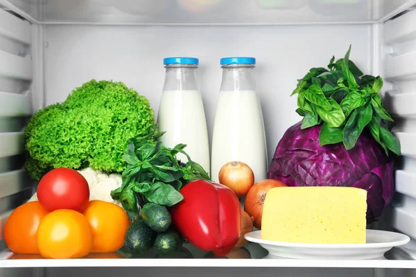 Open fridge full of vegetables with cheese and bottle of milk