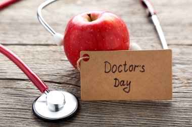 Yazıt doktorlar gün ahşap masa stetoskop ve Kırmızı elma ile