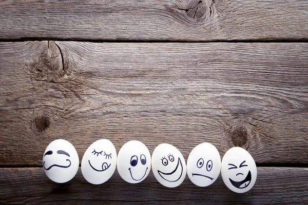 Eggs with funny faces on grey wooden table