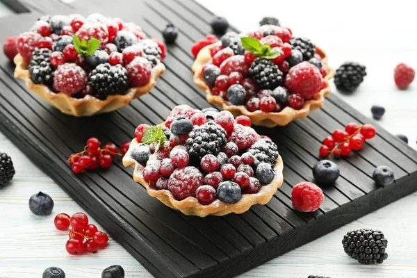 Tasty tartlet with berries and powdered sugar on white wooden table