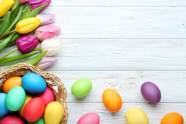 五颜六色的复活节彩蛋在篮子与郁金香在木桌上 — 图库照片
